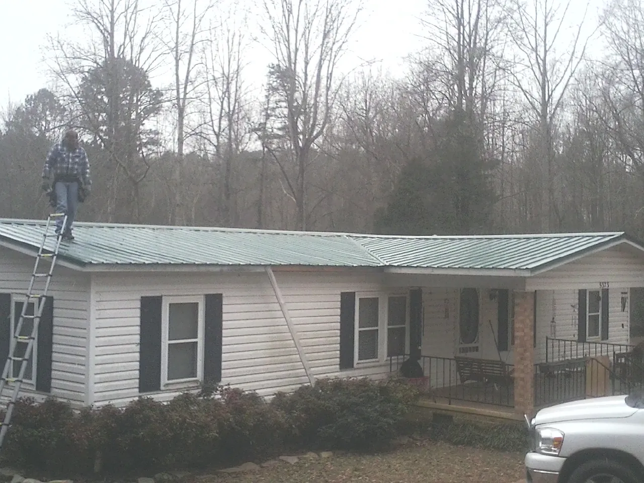 Worker on a ladder beside a new green metal roof on a ranch home in Mineral Point