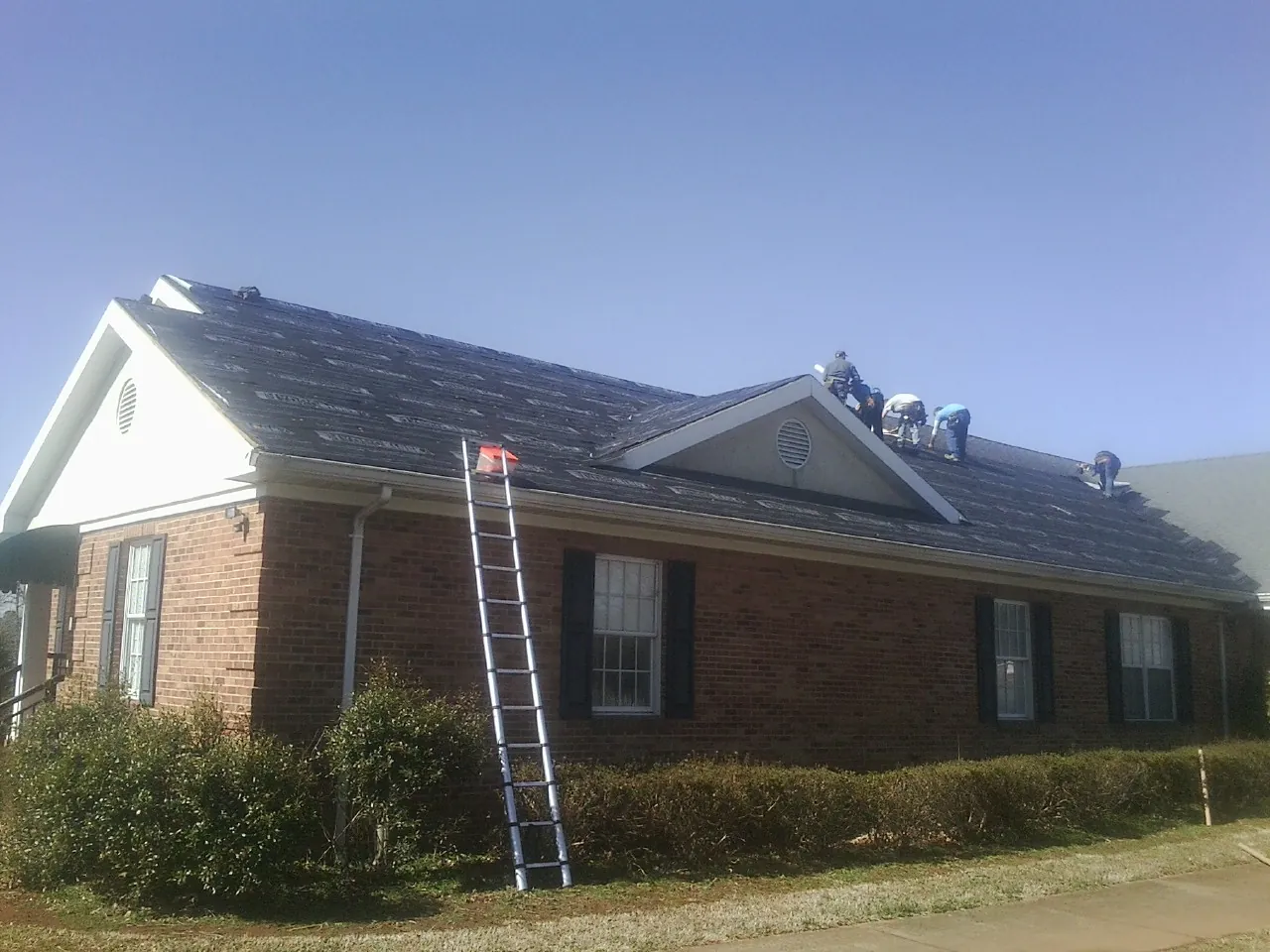 Crew tearing shingles off a brick ranch roof with a ladder set — Emergency Roof Repair work by our crew in Mineral Point
