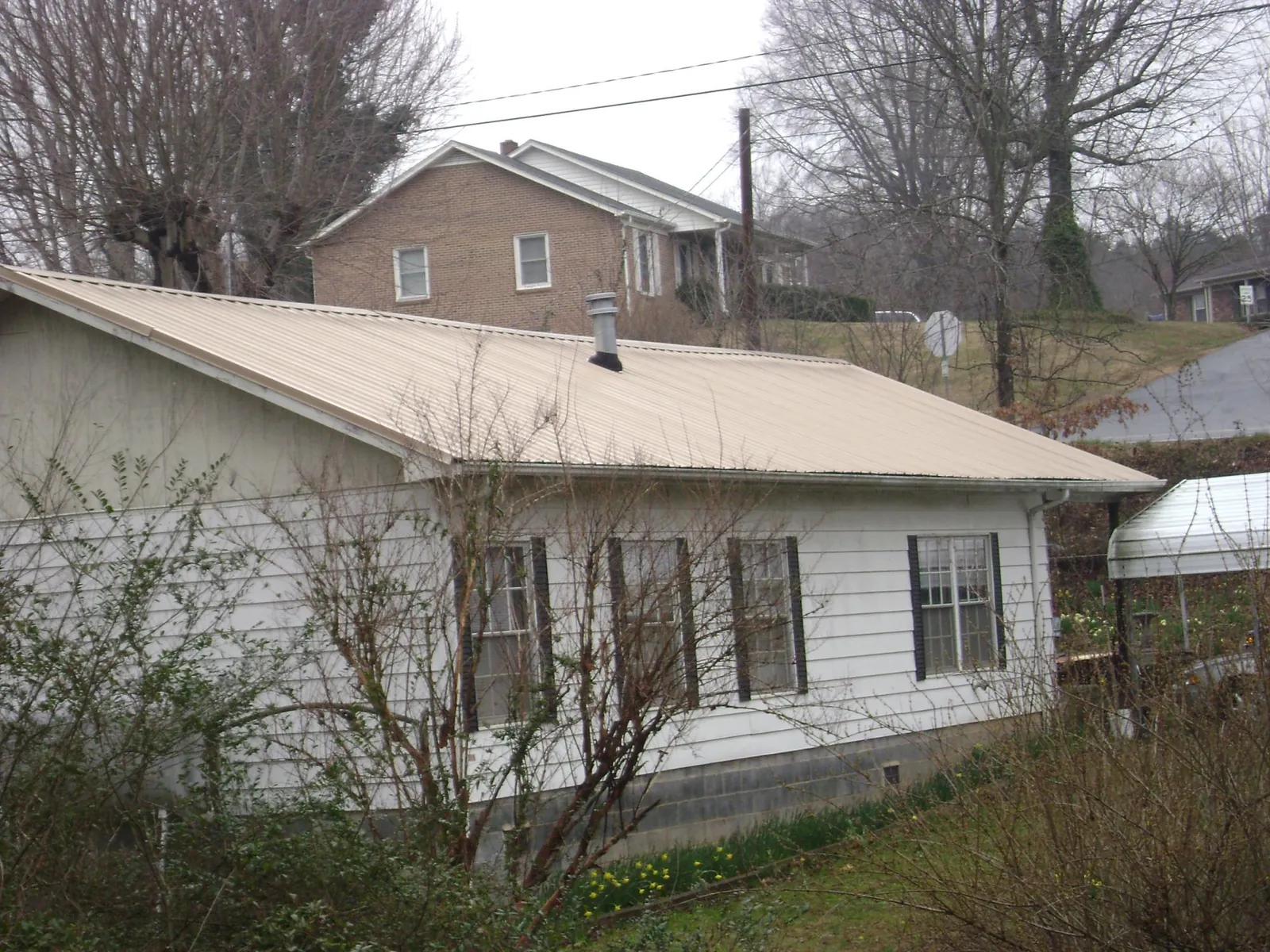 Tan metal roof on a white sided house set into a hillside — Commercial Roofing by Roofing Brothers in Mineral Point